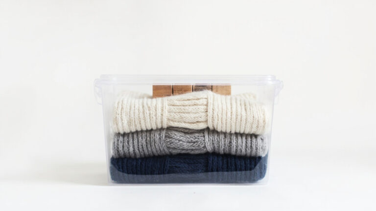 Folded wool sweaters stored in airtight container with cedar blocks for moth prevention