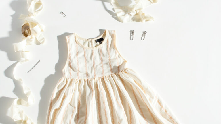 Summer dress with no-sew alteration supplies including fabric tape, needle and thread, and safety pins on a white surface
