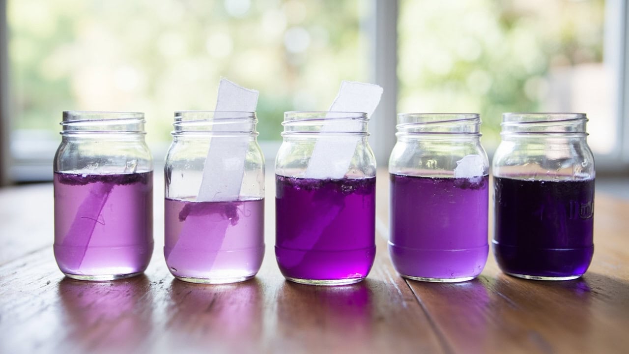 Diagram showing five containers with progressively darker purple dye baths with a fabric strip being dipped to different depths to create ombre gradient
