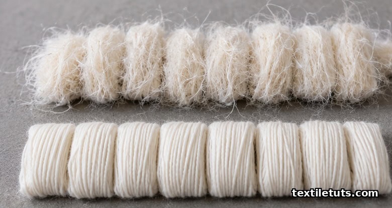 Side-by-side rows of carded and combed cotton yarn samples on a neutral inspection table, showing surface fuzz versus smooth fiber alignment.