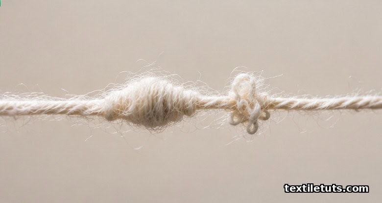 Macro view of cotton ring-spun yarn showing a slub swell, a small tangled nep, and a thinner section along the strand.