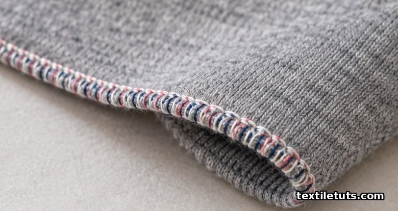 Heather grey jersey knit edge finished with a narrow rolled serger hem in multi-colored overlock thread