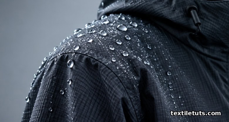 Technical rain-shell jacket with water droplets beading and rolling off the dark ripstop face fabric.