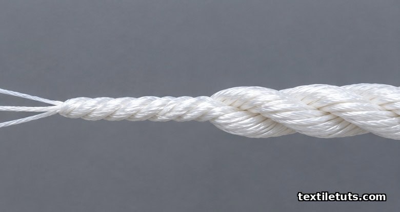 Close-up of plied industrial yarn showing three Z-twist single filaments cabled together in the opposite S-twist direction on a grey background.