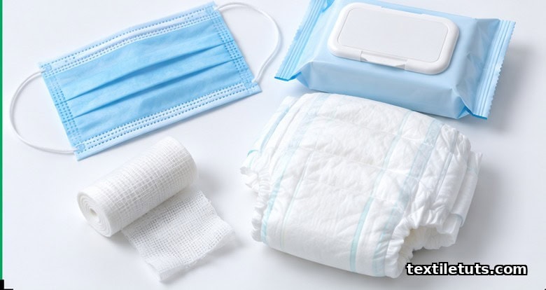 Flat-lay of nonwoven end-use products including a blue face mask, baby wipes pack, folded diaper, and medical gauze roll.