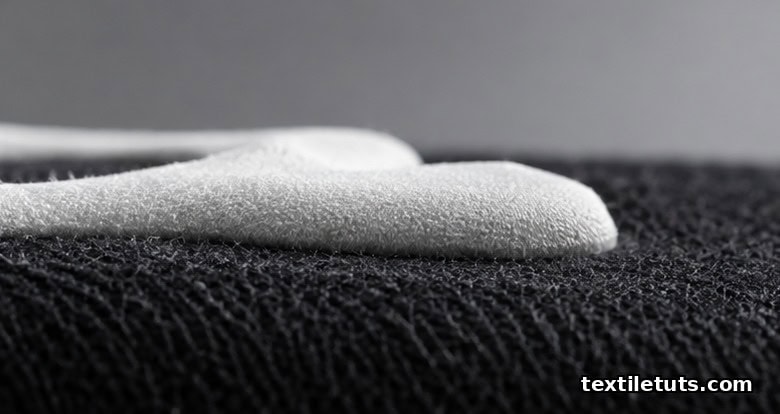 Side-profile macro of a raised puff ink layer on a black cotton hoodie showing dimensional lift above the fabric.