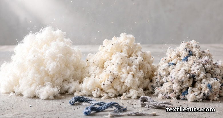 Loose off-white recycled cotton fiber tufts piled on a matte workbench under soft daylight.