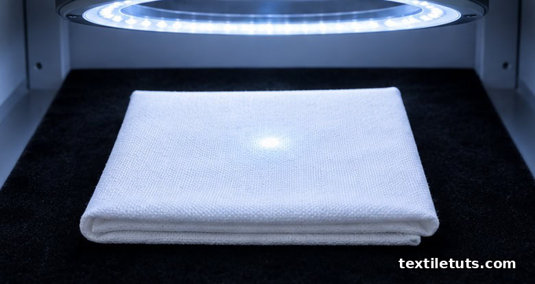 Folded bleached cotton fabric under a D65 daylight simulator ring light for CIE whiteness index measurement.