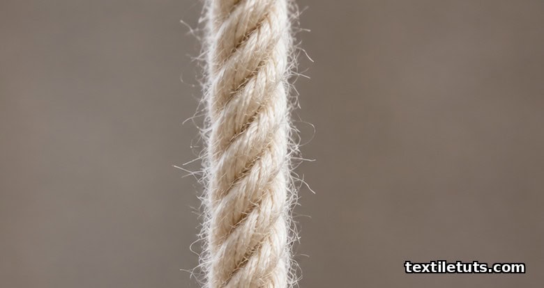 Macro close-up of a single cotton yarn held vertically showing diagonal fiber bands sloping upward from left to right.