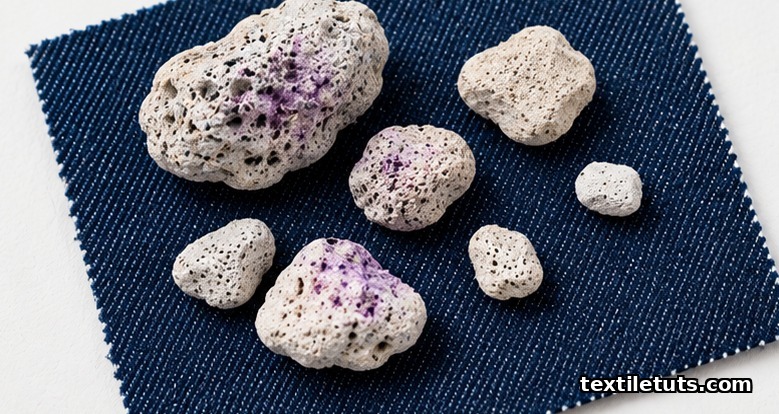 Rough white pumice stones of varying sizes resting on indigo denim twill fabric, a few stained faint purple from permanganate.