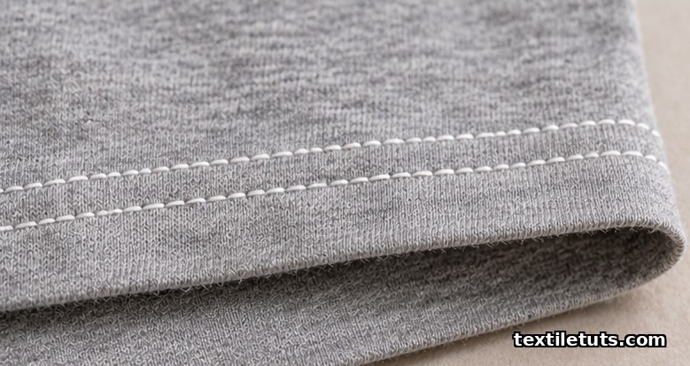 Close-up of a finished T-shirt hem with two parallel rows of coverstitch topstitching on heather gray knit fabric.